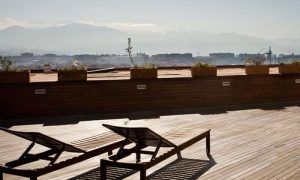 Una terraza de madera con dos tumbonas ofrece la tranquilidad de un solárium bajo un cielo despejado con vistas al paisaje urbano y a las montañas distantes, similar al Spa con solárium para 2 parejas en Barceló Granada Congress. - ForTwo - Planes para parejas