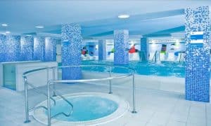La zona de piscina cubierta del Hotel Gala, Tenerife, cuenta con elegantes mosaicos azules, una bañera de hidromasaje redonda ideal para una experiencia de sesión de spa en pareja y piscinas más grandes que se extienden con gracia en el fondo. - ForTwo - Planes para parejas