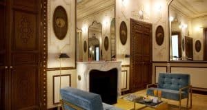 Descubra la suite Preciosa del Hotel Axel - Solo Adultos (Madrid), donde paredes ornamentadas, una chimenea de mármol y lujosos sillones de terciopelo azul crean un ambiente elegante. Una pequeña mesa con refrigerios realza el sofisticado encanto de este exclusivo refugio. - ForTwo - Planes para parejas