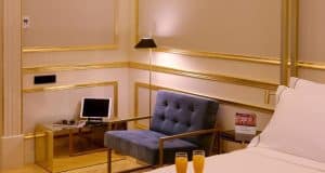 Experimente la sofisticación en la Suite Preciosa del Hotel Axel, Madrid - Solo Adultos. Disfrute de una silla de terciopelo azul, una mesita de noche, una tableta moderna, una lámpara de ambiente y dos vasos de zumo de naranja natural. - ForTwo - Planes para parejas