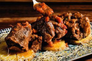 Este tierno guiso de ternera sobre patatas laminadas, coronado con brotes y servido con cuchara, ofrece un exquisito sabor a Granada. Perfecto para una cena romántica en La Tabernilla del Darro. - ForTwo - Planes para parejas