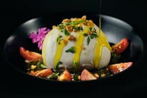 Disfrute de una cena romántica en La Tabernilla del Darro en Granada con queso burrata adornado con hierbas y nueces, rodeado de gajos de tomate y flores moradas, rociado con aceite. - ForTwo - Planes para parejas