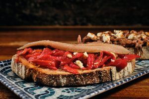 Disfrute de la Cena romántica en La Tabernilla del Darro en Granada, con pimiento rojo asado y pescado sobre pan rústico, bellamente servido en un plato estampado. - ForTwo - Planes para parejas