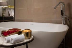 La Suite Presidencial del hotel Meliá Castilla (Madrid) cuenta con un lujoso baño con bañera blanca, pétalos de rosa, una vela encendida y toallas enrolladas sobre una pintoresca mesa. - ForTwo - Planes para parejas