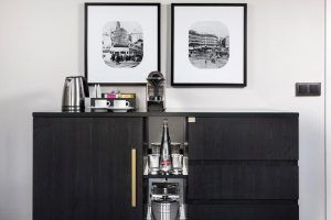En la Suite Presidencial del Hotel Meliá Castilla de Madrid, un mueble negro alberga una cafetera, una tetera, fotos de Madrid enmarcadas encima y un minibar extraíble con botellas. - ForTwo - Planes para parejas