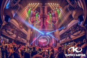 La vibrante escena de discoteca, repleta de luces de colores y una multitud animada, gira en torno a un gran escenario circular que muestra con orgullo "Discoteca Kapital (Madrid)", el emblemático lugar de moda. - ForTwo - Planes para parejas