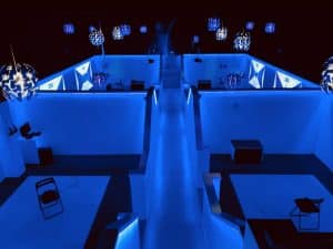 Explora la Realidad Virtual en Pareja en Oasis VR Experience en San Sebastián de los Reyes, Madrid. Una sala futurista con luces azules y lámparas geométricas crea el ambiente, mientras que las gafas de realidad virtual sobre bancos te esperan para transportarte a reinos inimaginables. - ForTwo - Planes para parejas