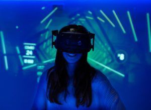 Una persona en Realidad Virtual en Pareja en Oasis VR Experience (San Sebastián de los Reyes, Madrid) lleva un casco rodeado de luz azul y gráficos digitales, mostrando el futuro de la realidad virtual. - ForTwo - Planes para parejas
