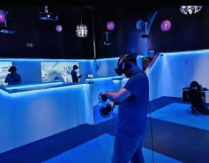 En la "Realidad Virtual en Pareja en Oasis VR Experience" en San Sebastián de los Reyes, Madrid, los participantes utilizan gafas y controladores de realidad virtual en una sala iluminada con neón, suelos azules y orbes brillantes. - ForTwo - Planes para parejas
