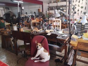 Un perro se sienta en una silla en un animado taller de Barcelona, repleto de herramientas y materiales, ofreciendo una auténtica "Experiencia Joyero por un día". - ForTwo - Planes para parejas