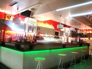 Este elegante y moderno bar con mostrador iluminado en verde, taburetes y botellas iluminadas ofrece Combinado de mojitos y pintxos únicos (Bilbao) para una velada vibrante llena del sabor de Bilbao. - ForTwo - Planes para parejas