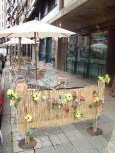 Disfrute de mojitos y pintxos únicos en una encantadora cafetería al aire libre en Bilbao, que cuenta con asientos en la acera con mesas y una cerca de mimbre adornada con flores. - ForTwo - Planes para parejas
