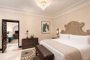 Máxima elegancia en la Suite Deluxe del hotel Alfonso XIII (Sevilla) ofrece una experiencia elegante con gran cama, candelabro ornamentado y decoraciones con estilo. Una puerta conduce a un salón íntimo, perfecto para relajarse. - ForTwo - Planes para parejas