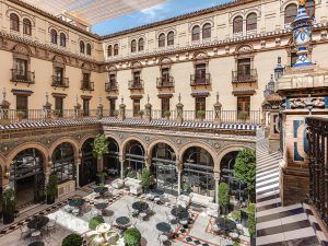 Explore el histórico patio del Hotel Alfonso XIII en Sevilla, con arcos, azulejos decorativos y terrazas. Rodeado por un edificio de varias plantas con alojamientos Máxima elegancia en la Suite Deluxe, este encantador espacio personifica el lujo. - ForTwo - Planes para parejas