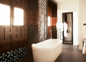 Descubra el encanto del baño moderno en las Suites únicas en el Hotel Palacio De Villapanés (Sevilla) con una elegante bañera independiente blanca, elegantes contraventanas de madera, un elegante espejo de pared, una lujosa bata y exquisitos azulejos decorativos. - ForTwo - Planes para parejas
