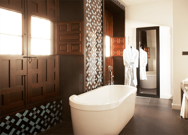 Descubra el encanto del baño moderno en las Suites únicas en el Hotel Palacio De Villapanés (Sevilla) con una elegante bañera independiente blanca, elegantes contraventanas de madera, un elegante espejo de pared, una lujosa bata y exquisitos azulejos decorativos. - ForTwo - Planes para parejas