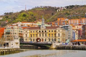 Descubra el edificio histórico con su torre del reloj junto al río, en medio del vibrante paisaje urbano y las verdes colinas de Bilbao. Disfrute de impresionantes vistas desde el Funicular de Artxanda o explore con nuestro "Tour guiado + funicular de Artxanda (Bilbao)". - ForTwo - Planes para parejas