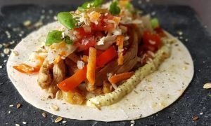 Tortilla abierta cubierta con suculento pollo, vibrantes pimientos rojos, repollo rallado y semillas, haciendo eco de los exquisitos sabores del Menú para dos de La Factoría de Parrilla García en Tenerife. - ForTwo - Planes para parejas