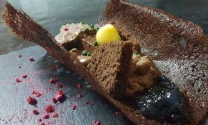 Disfrute de un postre de chocolate gourmet con una rica mousse, crujiente y delicadas guarniciones, servido a la perfección en un plato de pizarra. Ideal para compartir, este tentador capricho forma parte de nuestro exclusivo Menú para dos en La Factoría de Parrilla García en Tenerife. - ForTwo - Planes para parejas