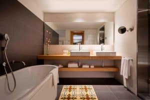 Experimente la elegancia de un baño moderno en la Suite Grand Terrace, la comodidad hecha habitación (Barcelona), con lavabos dobles, un amplio espejo, una acogedora bañera y una alfombra estampada para relajarse. Este lujoso oasis realza su sofisticada estancia. - ForTwo - Planes para parejas
