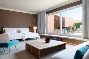 Sienta la comodidad de una moderna Suite Grand Terrace, la comodidad hecha habitación en Barcelona, que cuenta con dos camas, una mesa de centro de madera y un gran ventanal en la terraza con acogedoras sillas. - ForTwo - Planes para parejas