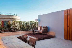 Disfrute de la comodidad de Suite Grand Terrace, la comodidad hecha habitación (Barcelona), relajándose en el patio de la azotea con zona de estar, sillas de madera, una mesa y exuberantes plantas bajo un cielo azul claro. - ForTwo - Planes para parejas