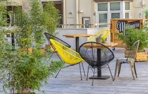 El patio al aire libre del Hostel Bcool Bilbao cuenta con modernas sillas amarillas y negras, mesas de madera y exuberante vegetación, creando un refugio refrescante en el corazón de la ciudad. - ForTwo - Planes para parejas