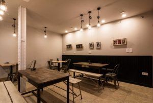El Hostal Bcool Bilbao cuenta con un acogedor interior de cafetería con mesas de madera, bancos y lámparas colgantes. Las fotos enmarcadas en las paredes contribuyen a la cálida atmósfera, plasmando la esencia de Bilbao. - ForTwo - Planes para parejas