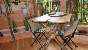 Una mesa rústica única de madera con dos sillas plegables evoca el encanto estilo casa en el árbol de "Habitaciones únicas en Cabañas en los árboles (Vizcaya)", rodeada de vegetación y decoración natural. - ForTwo - Planes para parejas