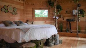 Un acogedor dormitorio rústico con paredes de madera, decoración de tocones de árboles y una cama con sábanas blancas es un ejemplo de las habitaciones únicas que ofrece Cabañas en los árboles (Vizcaya). - ForTwo - Planes para parejas