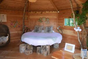 Disfrute de una estancia única en el acogedor interior de Habitaciones únicas en Cabañas en los árboles (Vizcaya), con una cama redonda, una silla colgante y taburetes de madera. Una pequeña ventana revela la exuberante vegetación exterior, capturando la esencia de los idílicos paisajes de Vizcaya. - ForTwo - Planes para parejas