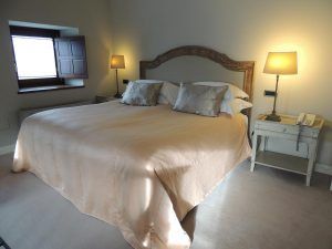 Una acogedora habitación del Hotel Castillo Del Bosque La Zoreda en Oviedo cuenta con una cama doble, mesas de noche con lámparas y ventanas con contraventanas de madera. - ForTwo - Planes para parejas
