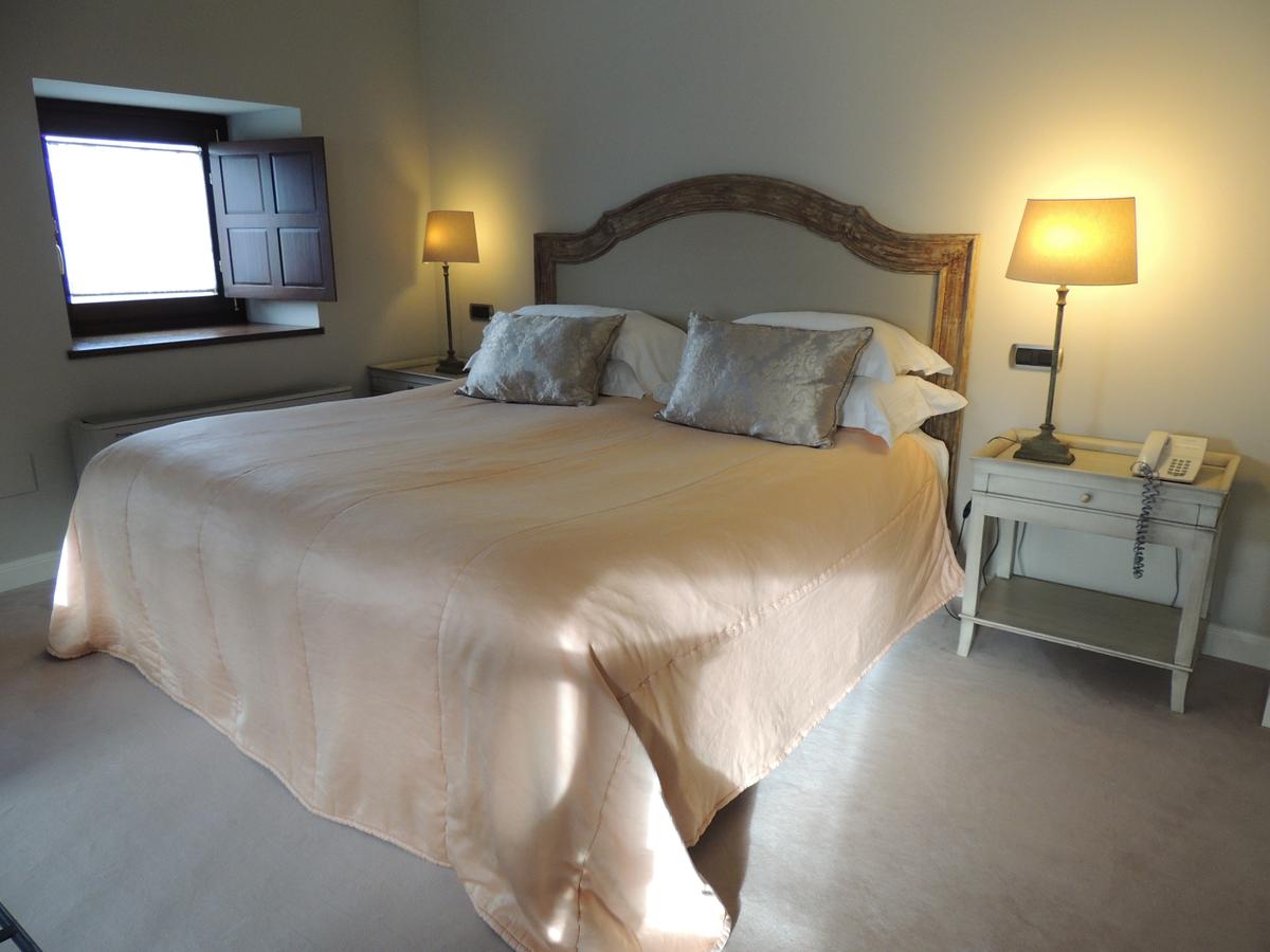 Una acogedora habitación del Hotel Castillo Del Bosque La Zoreda en Oviedo cuenta con una cama doble, mesas de noche con lámparas y ventanas con contraventanas de madera. - ForTwo - Planes para parejas