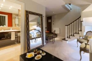 Descubra el encanto moderno del Hotel Castillo Del Bosque La Zoreda en Oviedo, donde unas elegantes escaleras y un gran espejo realzan una acogedora zona de estar con aperitivos, bebidas y un baño accesible cercano. - ForTwo - Planes para parejas