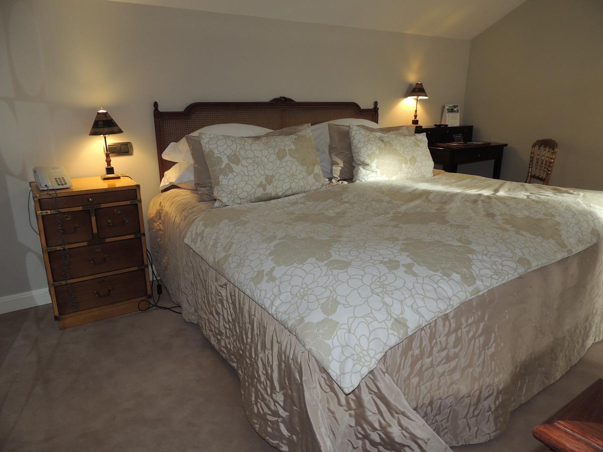 La acogedora habitación del Hotel Castillo Del Bosque La Zoreda en Oviedo ofrece una escapada encantadora con una cama grande con ropa de cama floral, mesitas de noche vintage, elegantes lámparas y un práctico escritorio de esquina. - ForTwo - Planes para parejas
