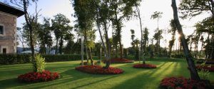 El Hotel Castillo Del Bosque La Zoreda de Oviedo cuenta con un exuberante jardín con árboles y parterres de flores de color rojo vivo, donde la luz del sol crea llamativas sombras sobre el césped. - ForTwo - Planes para parejas