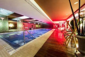 Relájese en el lujoso ambiente de la piscina cubierta del Hotel Castillo Del Bosque La Zoreda (Oviedo), que cuenta con una terraza de madera, tumbonas e iluminación ambiental. - ForTwo - Planes para parejas