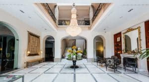 El vestíbulo del Hotel Castillo Del Bosque La Zoreda en Oviedo cuenta con una mesa central con girasoles, una gran lámpara de araña y unas intrincadas barandillas en los balcones. - ForTwo - Planes para parejas