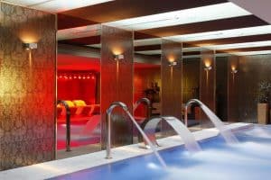 Experimente el lujo en el Hotel Castillo Del Bosque La Zoreda (Oviedo) con una piscina cubierta adornada con elegantes fuentes, iluminación moderna y lujosos sillones en un tranquilo entorno de spa. - ForTwo - Planes para parejas