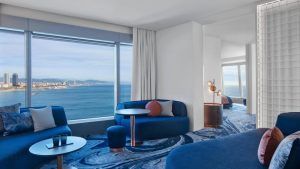 Descubra la Cool Corner Suite: el mar a tus pies en el Hotel W (Barcelona), donde el lujo moderno se fusiona con la modernidad. Esta exquisita habitación cuenta con sofás azules, una alfombra artística y amplios ventanales que ofrecen impresionantes vistas de la costa. - ForTwo - Planes para parejas