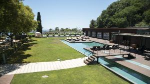 La piscina exterior del Hotel Miramar Barcelona ofrece cómodas tumbonas, frondosos árboles y una arquitectura moderna en un paisaje soleado. Disfrute de este entorno sereno desde la Gran Suite Mediterránea con terraza para un retiro perfecto. - ForTwo - Planes para parejas