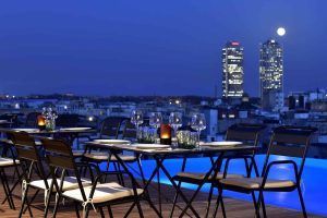 La Grand Suite, la joya de la corona del Grand Hotel Central (Barcelona), cuenta con un comedor en la azotea con impresionantes vistas del horizonte de la ciudad, con dos rascacielos iluminados bajo la luna llena. Experimente la magia del anochecer en este emblemático destino. - ForTwo - Planes para parejas