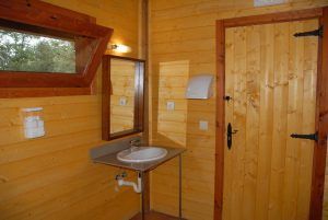 El baño de madera irradia un aire mágico con lavabo, espejo, dispensador de jabón y portarrollos. Una puerta de madera y una pequeña ventana ofrecen vistas a los encantadores árboles del exterior, que recuerdan a la Habitación mágica en los árboles de Cabanes Dosrius en Barcelona. - ForTwo - Planes para parejas