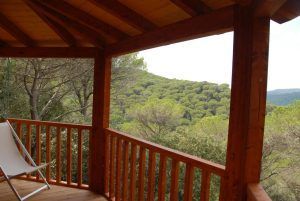 Una silla blanca sobre un porche de madera da a un frondoso bosque verde, evocando la encantadora esencia de la Habitación mágica en los árboles por Cabanes Dosrius (Barcelona). - ForTwo - Planes para parejas