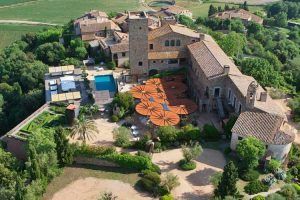 Vista aérea del Hotel Castell d'Emporda (Girona), una finca rústica que cuenta con una torre central, grandes sombrillas, exuberantes jardines y una acogedora piscina. - ForTwo - Planes para parejas