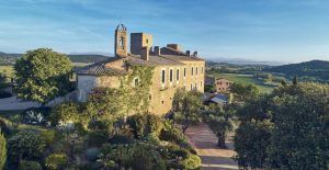 Situado en Girona, el Hotel Castell d'Emporda es una histórica estructura de piedra rodeada de frondosos árboles y jardines bajo un cielo azul claro. - ForTwo - Planes para parejas