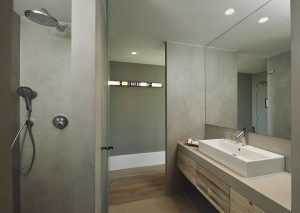El moderno baño del Hotel Castell d'Emporda (Girona) cuenta con paredes grises, una ducha, un lavabo con detalles en madera, un espejo grande y un cartel iluminado de Brighton. - ForTwo - Planes para parejas