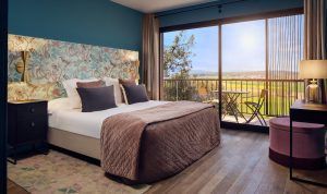 Un acogedor refugio en el Hotel Castell d'Emporda, Girona, con un cabecero floral, una gran ventana con vistas soleadas a Girona y asientos en el balcón. - ForTwo - Planes para parejas