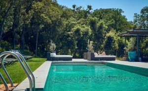 Bajo un cielo azul claro, un huésped se relaja en la piscina al aire libre del Hotel Castell d'Emporda en Girona, disfrutando de las tumbonas en medio de una serena belleza natural. - ForTwo - Planes para parejas