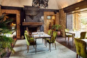 El elegante interior del Hotel Castell d'Emporda (Girona) cuenta con sillas verdes, mesas de madera, una chimenea de piedra y elementos de decoración rústica que crean un ambiente acogedor. - ForTwo - Planes para parejas